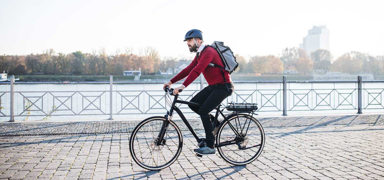 A man in a red sweater and helmet cycling to work along the embankment.